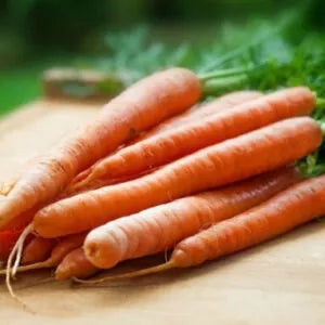 Several orange carrots are kept in a heap on a wooden table