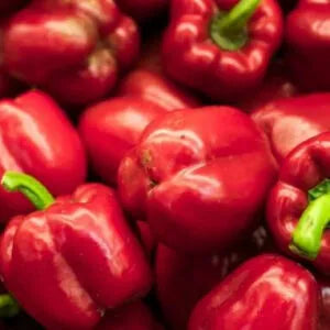 Many red capsicums with green stalks are kept in a heap on top of one another