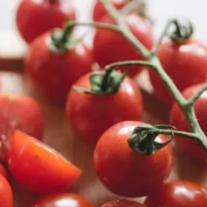 This is an image of many bright red cherry tomatoes on a branch with some tomatoes are cut into halves.