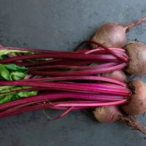 Several purplish beetroots with long leafy stalk bunched together in a black background