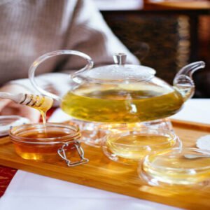 This is an image of a tea pot and two tea cups and also a small transparent bowl containing Raw Cider Honey kept on top of a table.