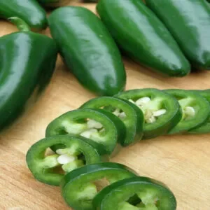 Chopped green chilli jalapeno kept on a wooden board with other whole jalapenos