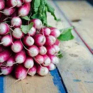 Small purple turnips kept together in a leafy bunch on a wooden platform