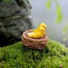 A cute Miniature Bird Nest on a lawn grass of terrarium with a bif stone in the background.
