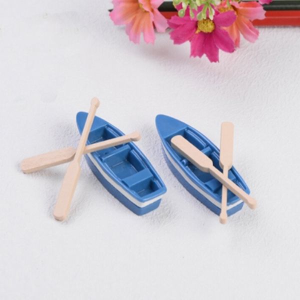 A beautiful and cute two Miniature boats with Oars on a white surface with some colored pencils and flowers beside them.