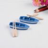A beautiful and cute two Miniature boats with Oars on a white surface with some colored pencils and flowers beside them.