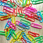 This is an image of multiple Multi colored paper clips against brown color background.