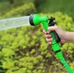 This is an image of a hand holding 7 Pattern Garden Hose Nozzle Water Spray Gun with greenery in background.